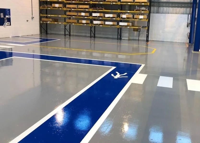 Área industrial com piso resinado contínuo e demarcação de circulação em azul e branco